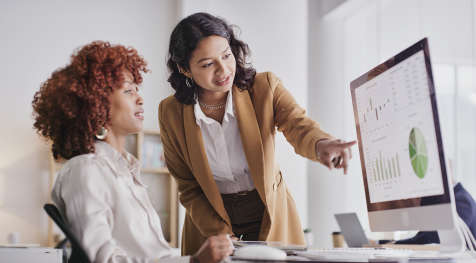 Two women look at data analytics on a computer screen