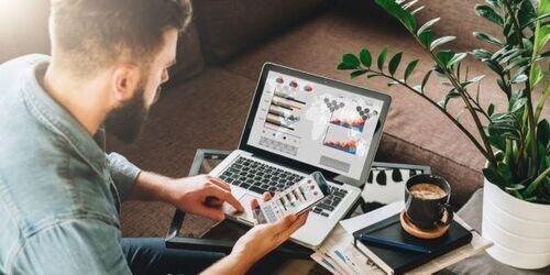 Man working on laptop with phone in hand. 