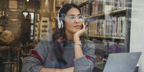 Woman sat in a library with a laptop. 