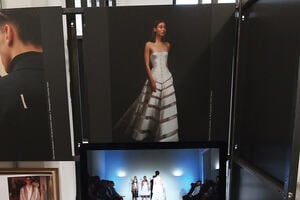 A photograph of a model posing wearing a white garment with a laptop on the table in front.