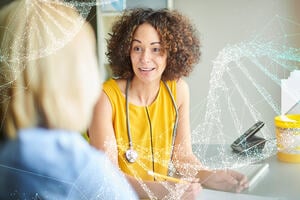 A female clinician in a yellow dress wearing a stethoscope speaks to a blonde female patient whose faced is obscured. A double helix is overlaid over the scene.