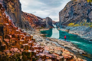 Person at the bottom of a canyon surrounded by basalt columns. View from flying drone of Studlagil Canyon.