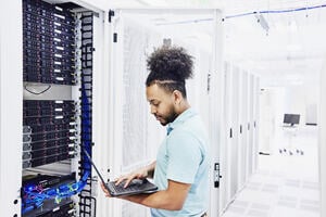 Man looking at a laptop while surrounded by servers.