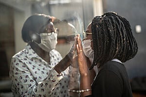 Two people either side of a clear plastic wall pressing their hands against each other.