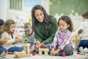 Learning facilitator helping children build a house out of wooden building blocks