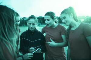 Sports coach holding clipboard talking to team of female football players