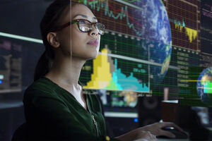 A young Asian woman looking at the global & environmental data projected on a see through display whilst seated in a dark office