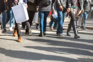 Abstract urban scene of busy city life. The curb is filled with multicultural people crossing while carrying shopping bags. Many punters are buying presents and taking advantage of special discount offers at city retail stores. Shallow focus.