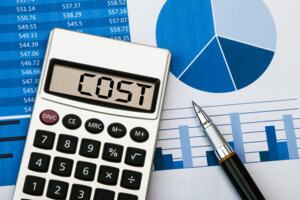 A calculator that reads 'Cost' with a pen next to it over a document displaying a blue pie chart, a table and a graph.