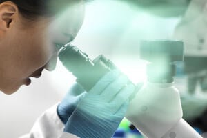 A close up shot of a female scientist conduction clinical research, as she looks down a microscope, studying rare diseases