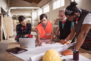 Female engineer directing her diverse team with architectural plan showing diversity and inclusion in construction and the built sector.