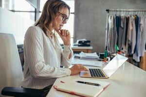 Woman in a office wear sat at her desk looking at her MacBook.