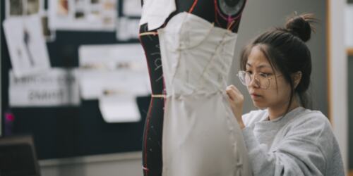 Woman sewing clothes onto a mannequin. 