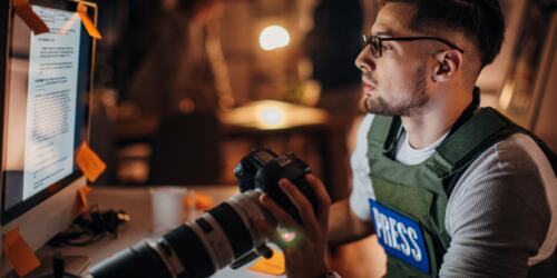 Man looking at PC screen with a camera in his hand. 