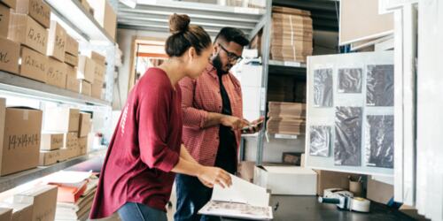 A man and woman working in a stock room filled with boxes.